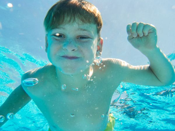 Funny boy swimming underwater looking at camera