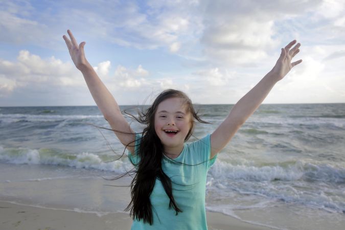 Happy child smiling with arms reaching up at the beach