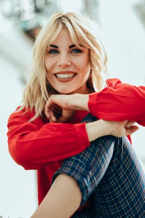Content blonde female with red shirt sitting with arms leaning on her knee, vertical