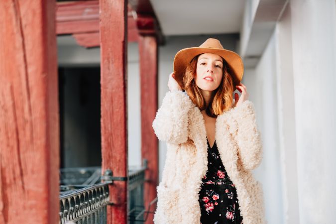 Smiling woman in warm wear standing near building and fence