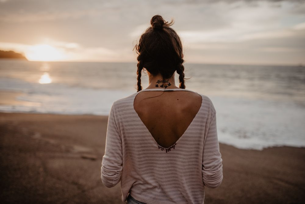 Anonymous female standing towards waving sea on sunset