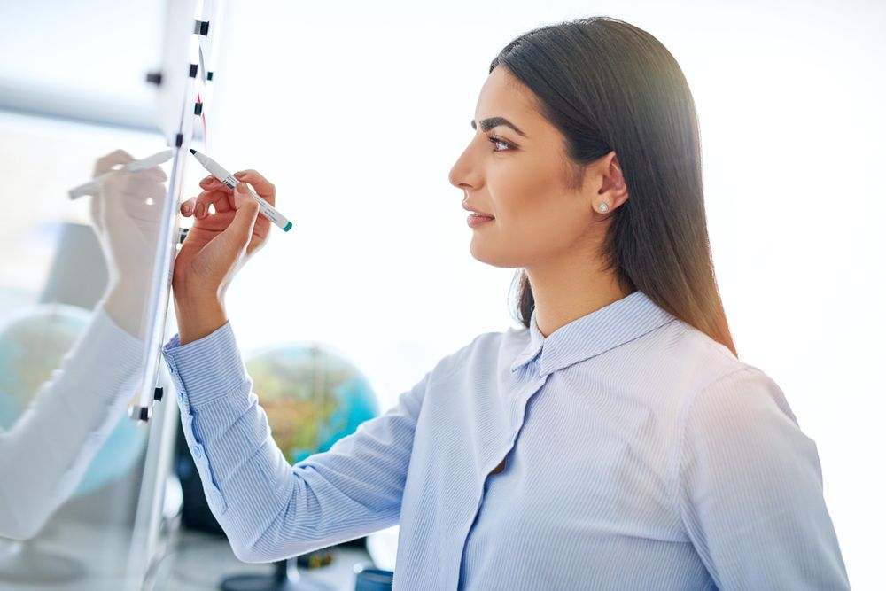 Arab woman writing on board working through problem for work