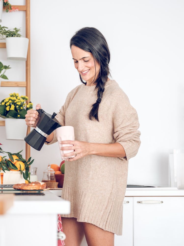 Positive female pouring hot coffee from moka pot in kitchen