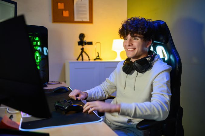 Happy young man sitting in front of monitor at table in room