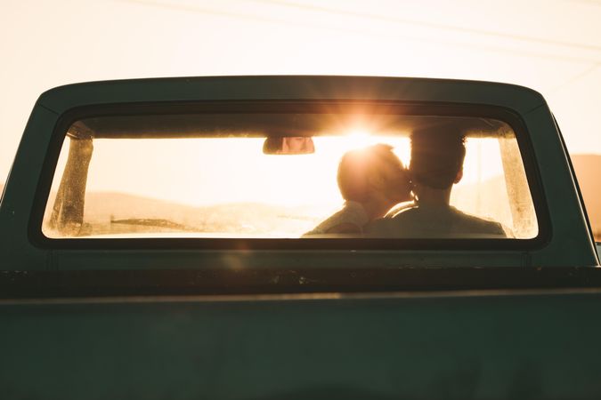 Woman with short hair kissing cheek of male sitting in driver seat of truck