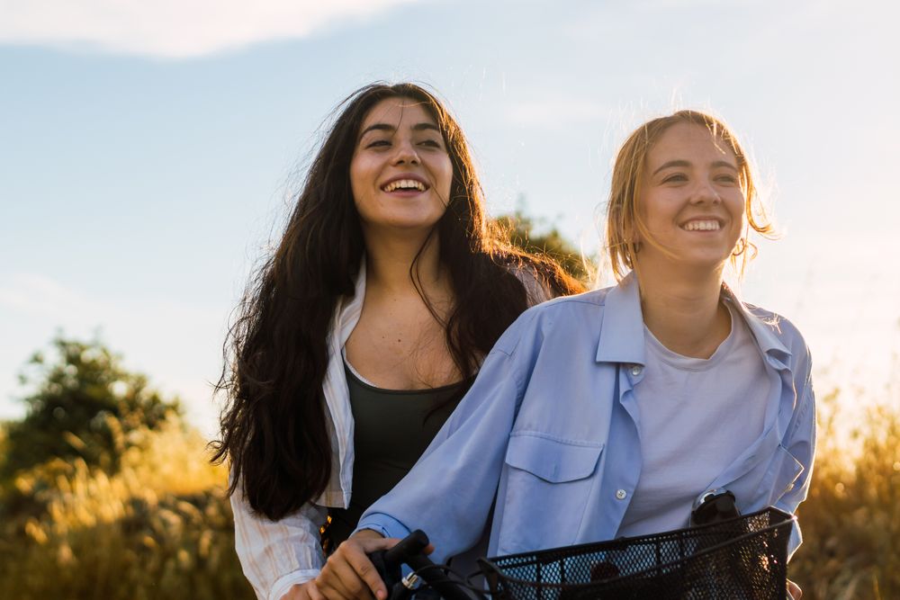 two young women on a bike in a field at sunset