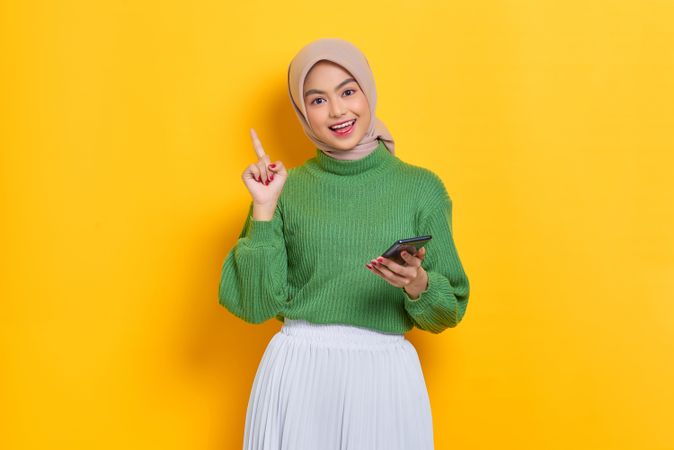 Smiling woman in headscarf holding up finger while holding on phone
