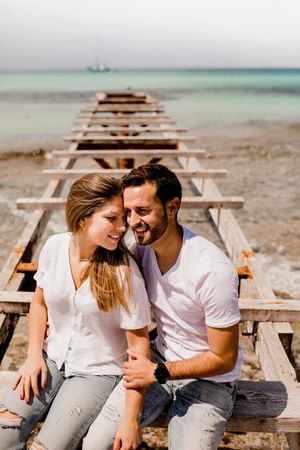 Glad lovers sitting on destroyed pier on seashore