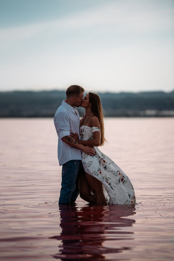 Side view of adorable couple embracing into an amazing beach with pink water