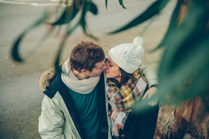 Affectionate couple in winter coats about to kiss under tree