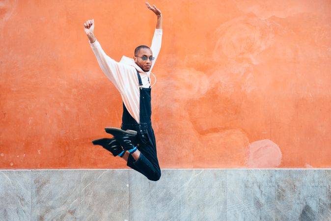 Male in overalls and hoodie jumping for joy in front of wall