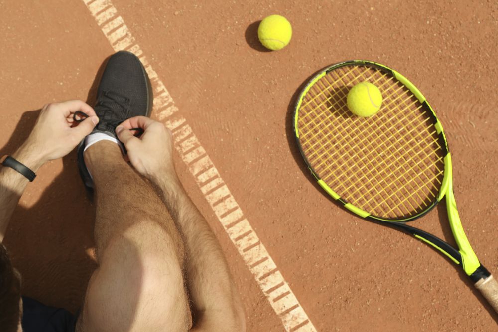 Man ties his shoelaces on clay court with racket and balls