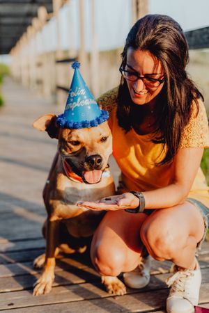 Smiling young woman petting brown dog in party hat