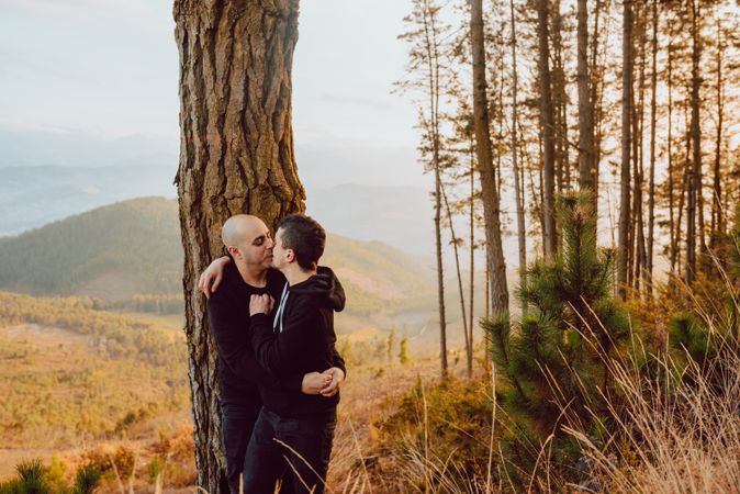 Smiling men hugging near tree in forest on hill