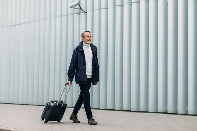Man walking with roller suitcase towards airport