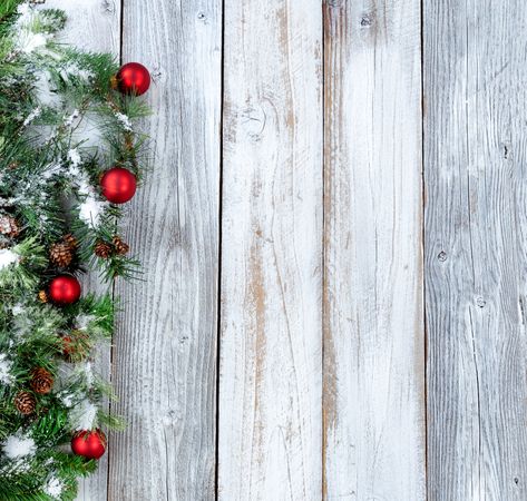 Christmas background with snowy evergreen branches and red ornaments on aged wood