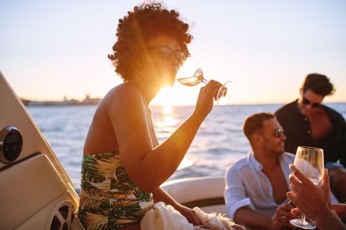 Woman with curly hair sipping white wine with sun setting in background