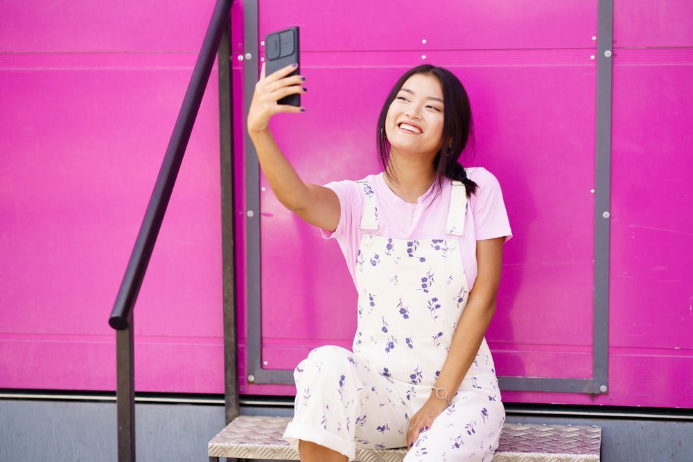 Smiling Chinese woman talking on video call on smart phone  sitting in front of pink trailer