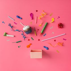 Gift box with colorful party items on pink background