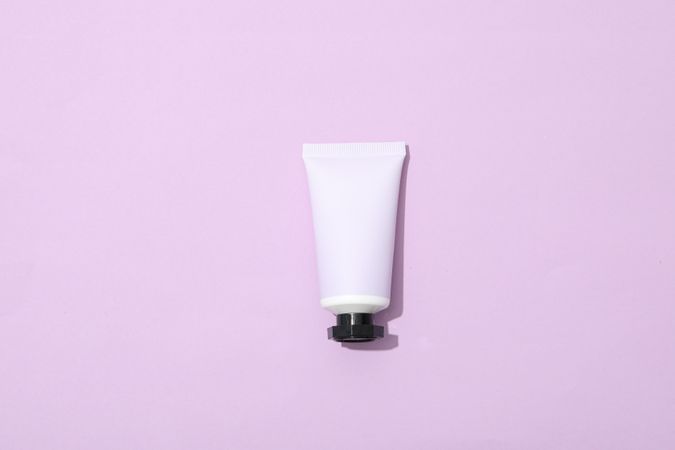 Tube with cream on pink background, top view