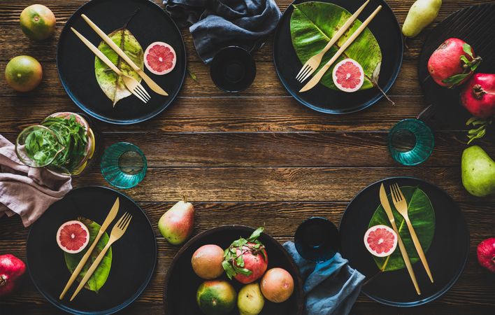 Fresh table setting with leaves on dark plates, with fruit on wooden table, with copy space