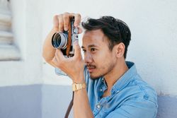 Asian man in blue shirt with short dark hair holding camera