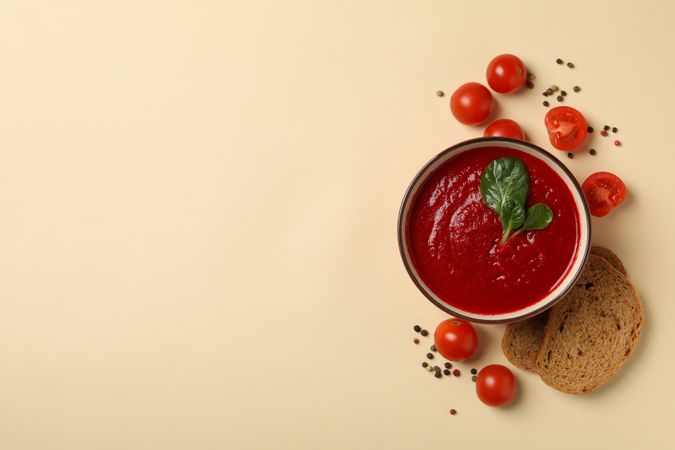 Top view of bowl of tomato soup with ingredients and slices of bread with copy space