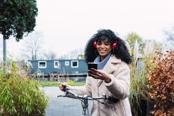 Delighted Black woman with smartphone on bicycle