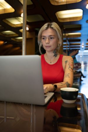 Tattooed young woman working on laptop computer in a coffee shop