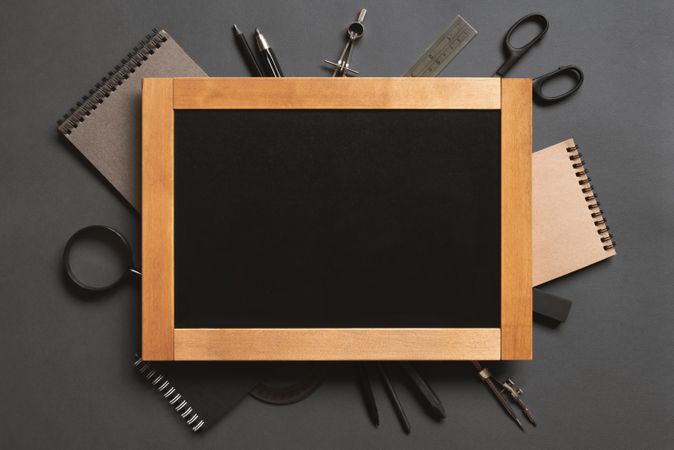 Framed writing board surrounded by stationary on dark background
