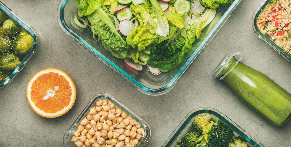 Variety of vegetable dishes in glass containers with bottles of dressing, wide composition