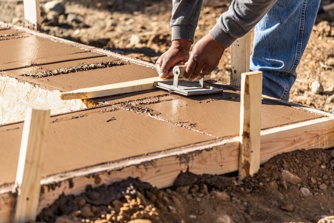 Construction Worker Using Hand Groover On Wet Cement Forming Coping Around New Pool