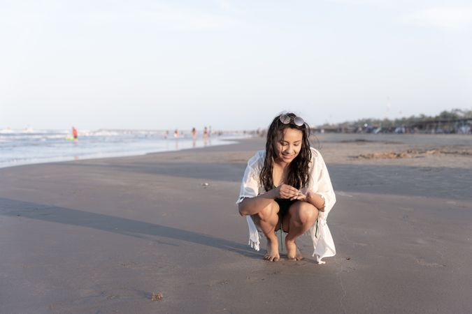 A young Hispanic woman is collecting seashells at the beach during sunset