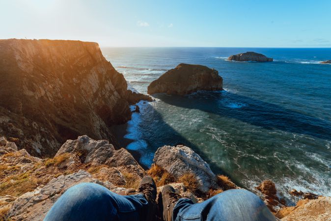 Person sitting on cliff near water