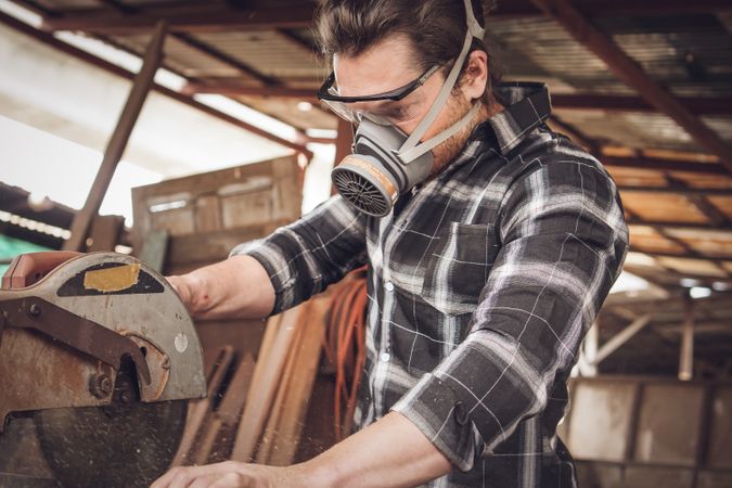 Male carpenter cutting wood board in workshop using electric saw 