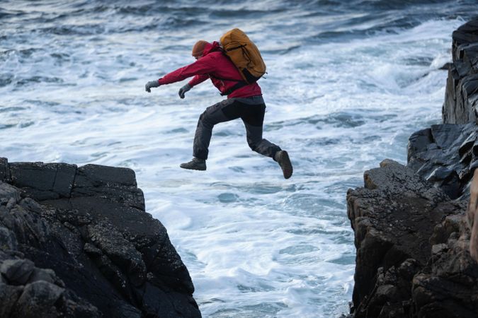 Person with backpack jumping from one cliff to another near ocean