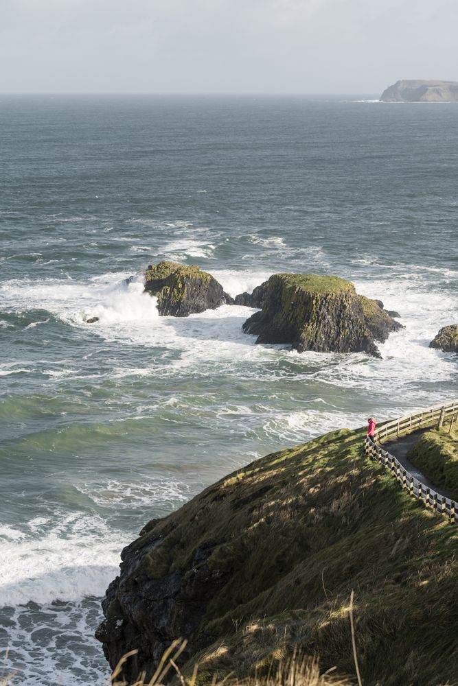 Person walking on country road between sea and field