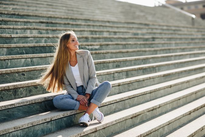 Carefree woman in blazer sitting on outdoor steps on sunny day