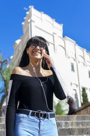 Young woman wearing earphones outdoors standing and listening to music looking away