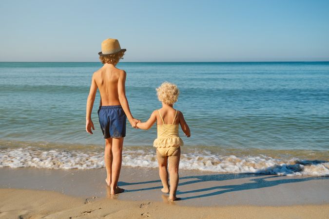 Children holding hands and walking on sandy beach