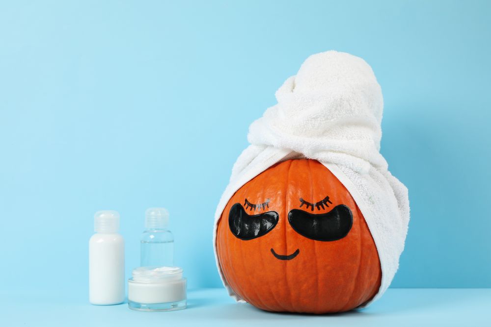 Skincare accessories and pumpkin with eye patches on blue background