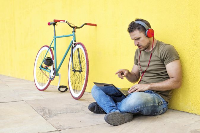 Male with red headphones sitting outside pointing at laptop