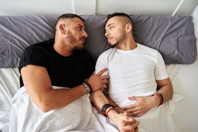 Smiling gay couple hugging on bed