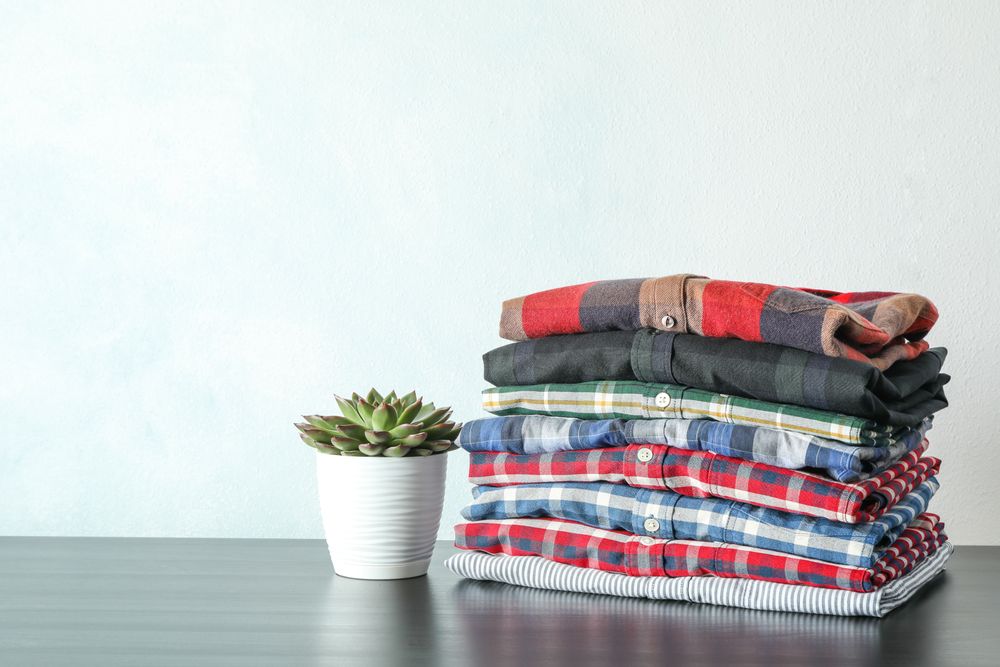 Stack of colorful shirts and succulent plant on table against light background