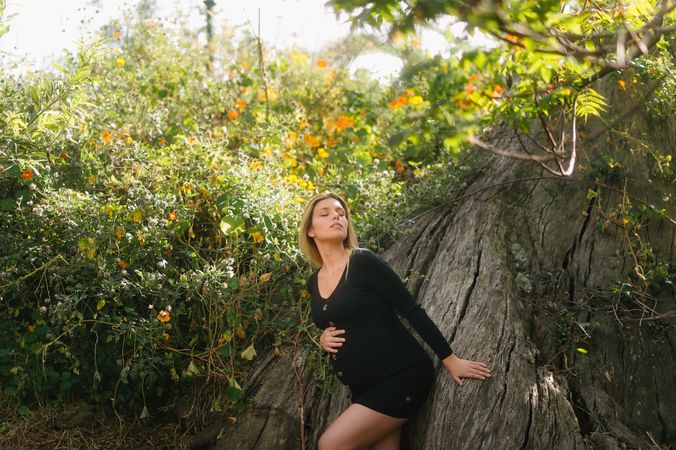 Pensive pregnant woman looking at camera while sitting in garden in sunny day