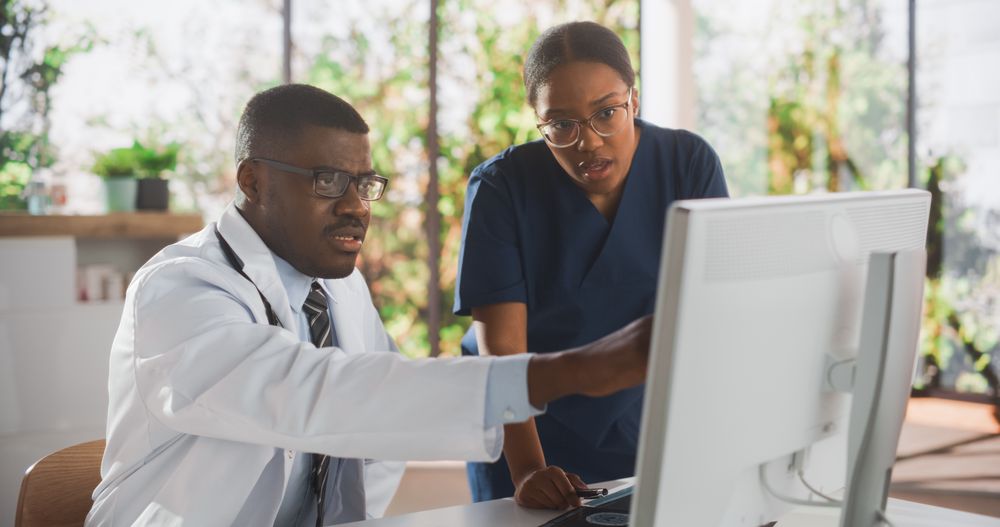 Professional Black Nurse and Doctor Having a Conversation, Using Computer, Discussing Patient Treatment, Drugs or Therapy