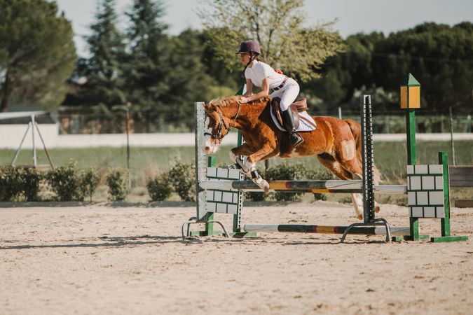 Teen girl riding horse and jumping over bars