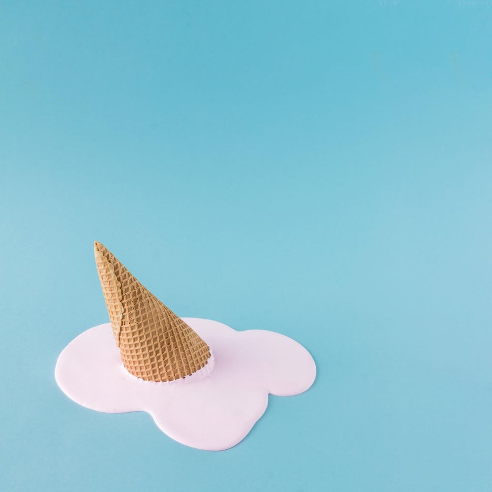 Melted pink ice cream and waffle cone on pastel blue background