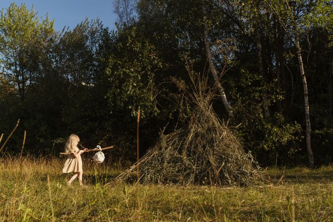 Girl carrying bindle in countryside near pile of dry twigs