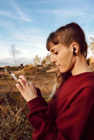 Young woman with piercing listening music on smartphone on hill